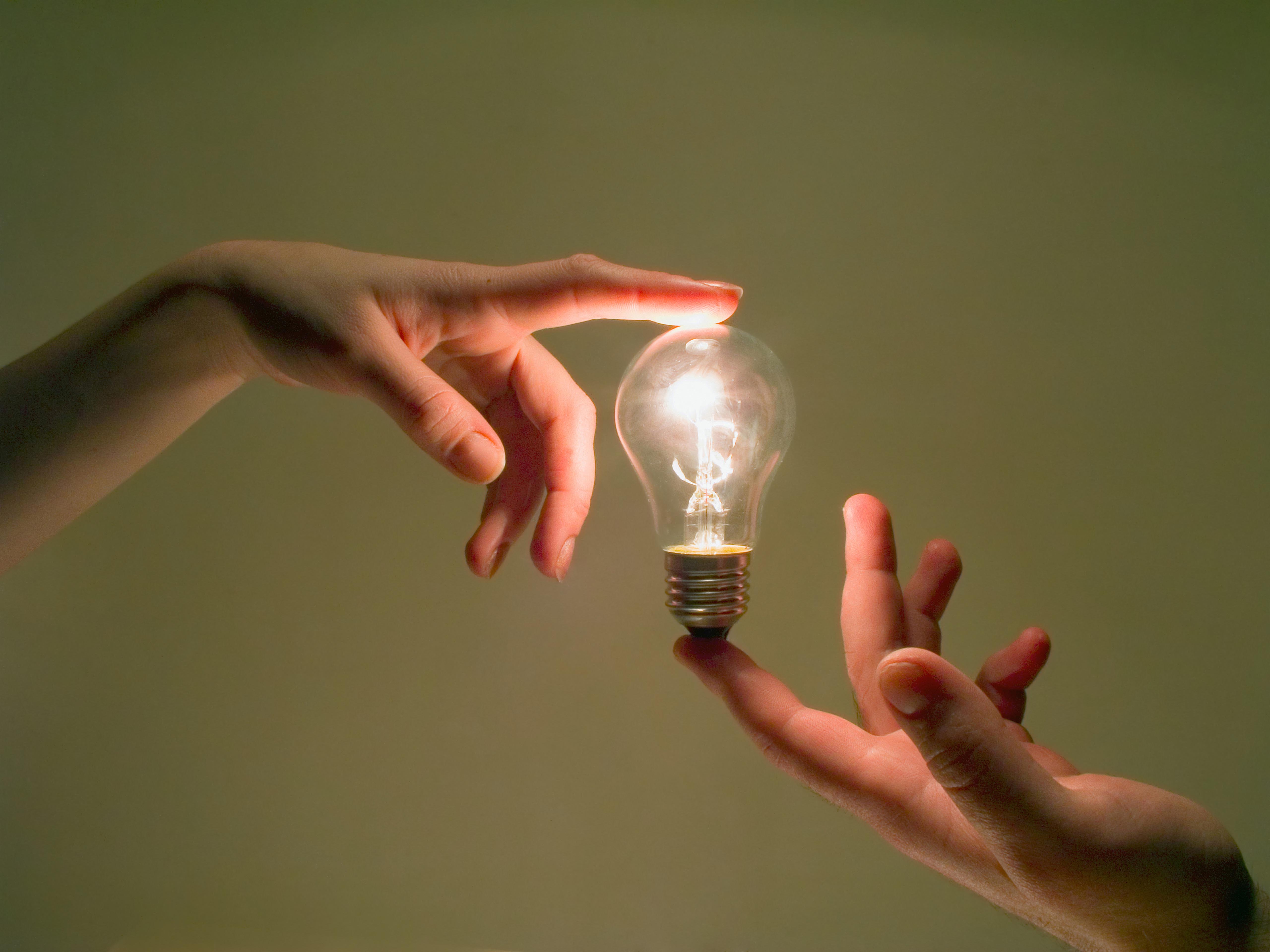 Two hands touching a light-bulb